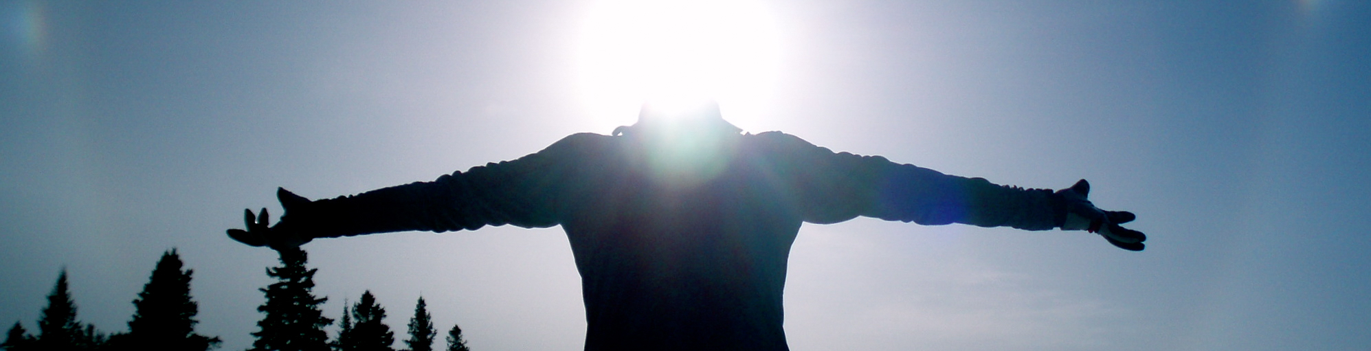 Silhouette of a person with their arms outstretched against the sun & sky
