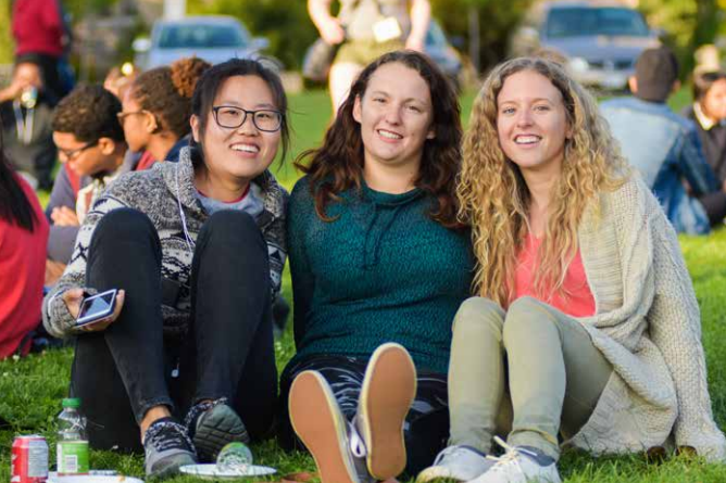 3 friends smile for the camera while sitting on Johnston Green