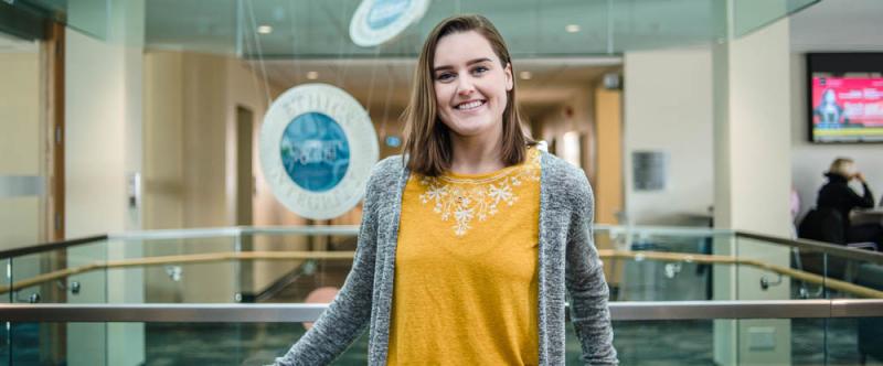 Portrait of graduate student Rebecca Pyrah (MA, History) in the atrium of MacDonald Stewart Hall at the University of Guelph  in the atrium of Mac Donald Stewart Hall at the University of Guelph