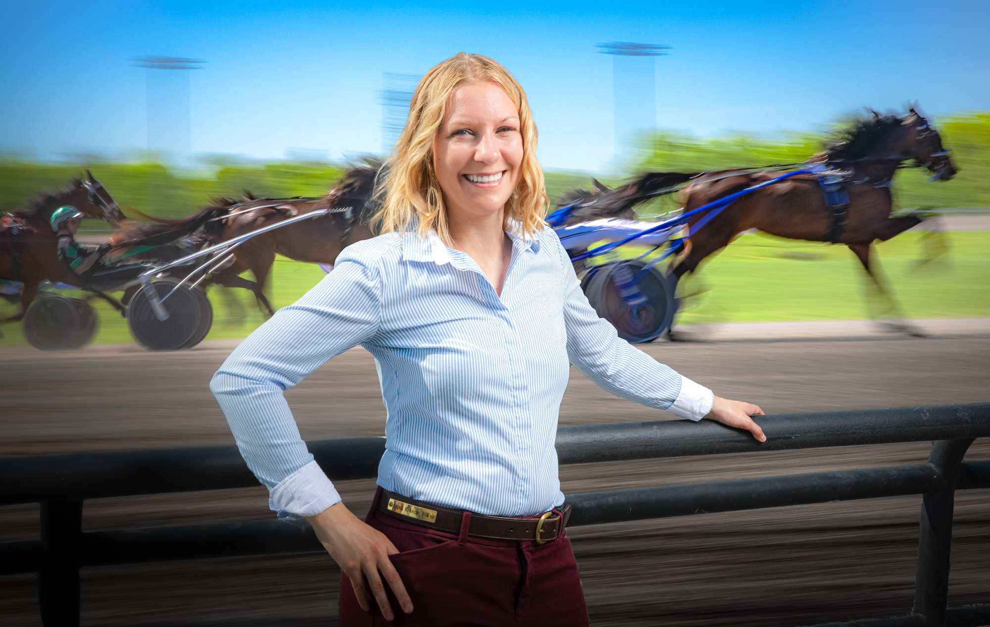 Portrait of Dr. Amanda Avison with standardbred horses racing behind her