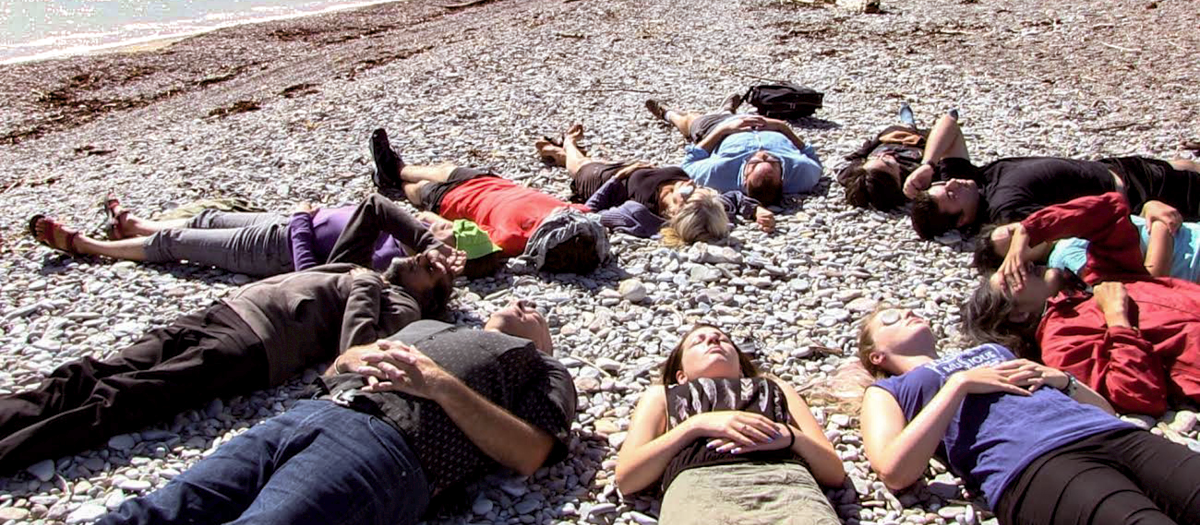 People lying in a circle on a pebble beach