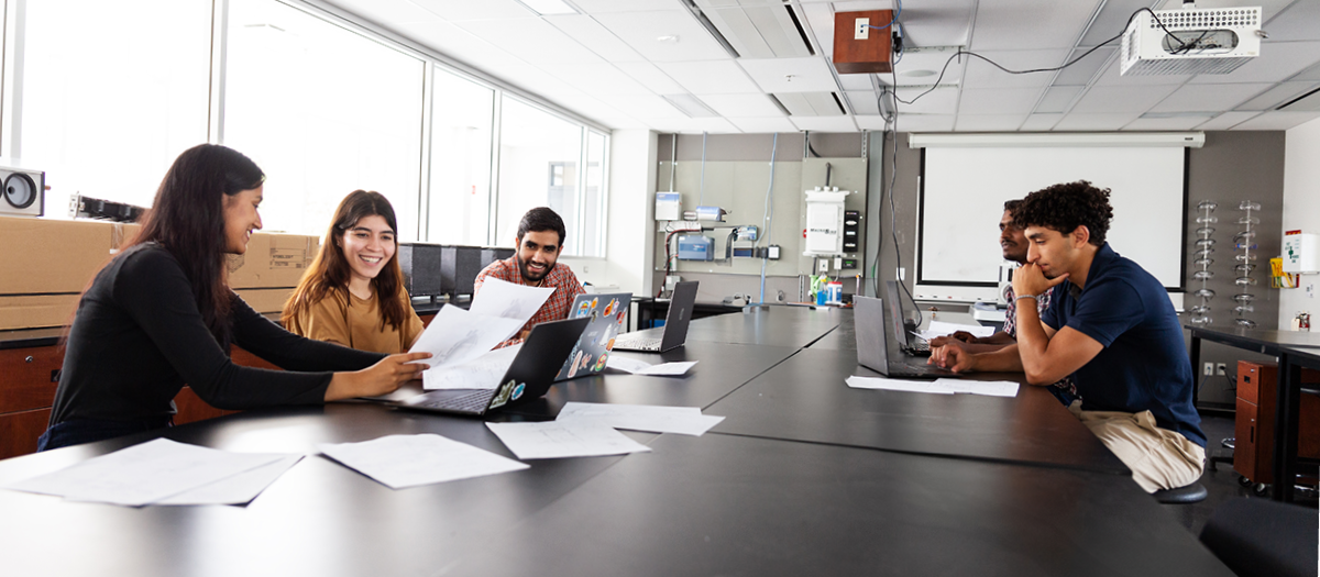 5 students collaborating around a lab table with computers