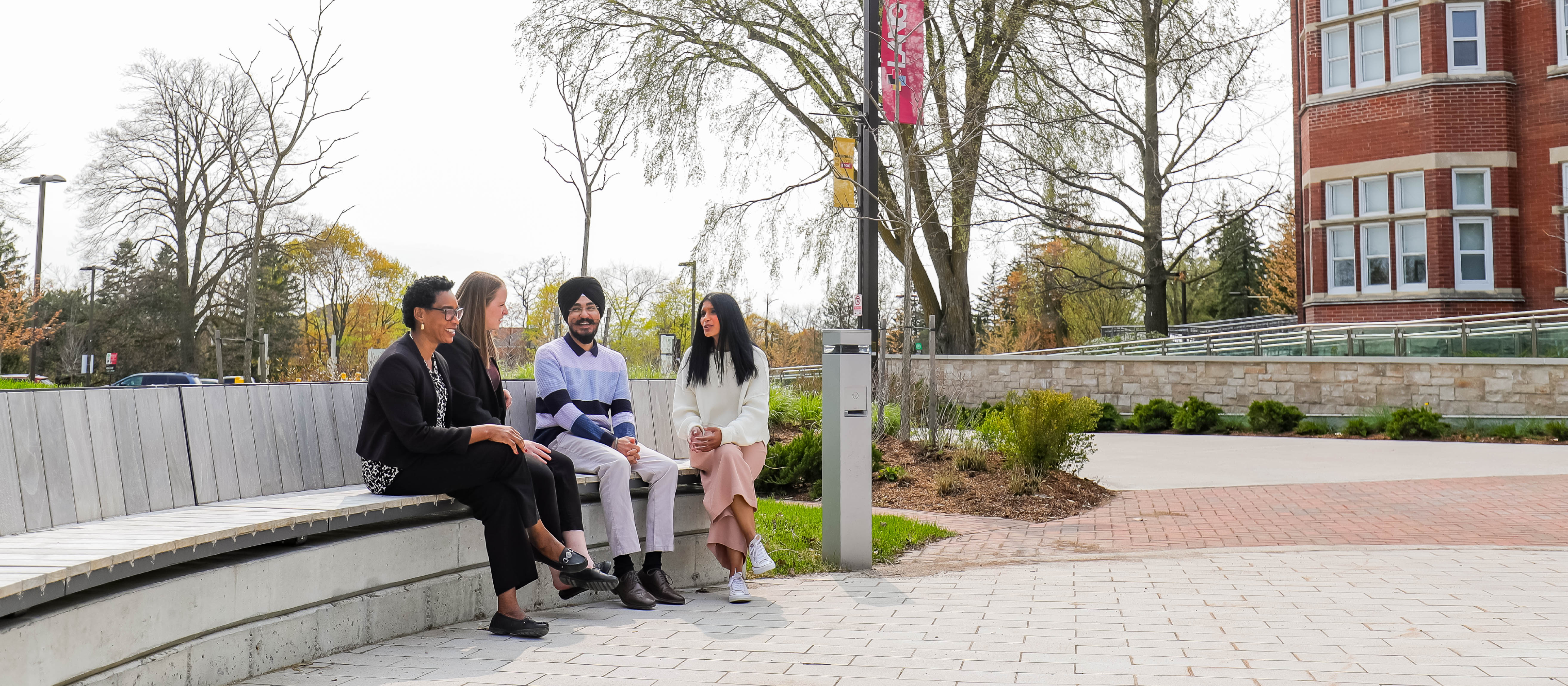 Four people chatting on a bench in front of the the Lang building