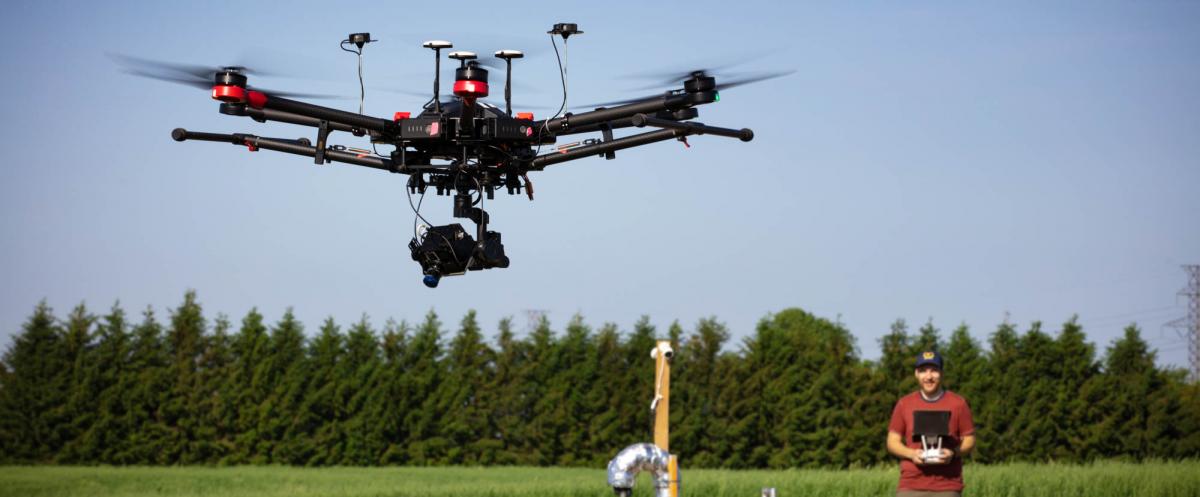 U of Guelph Geography grad student Bryce Miller operating a drone in a field of vegetation