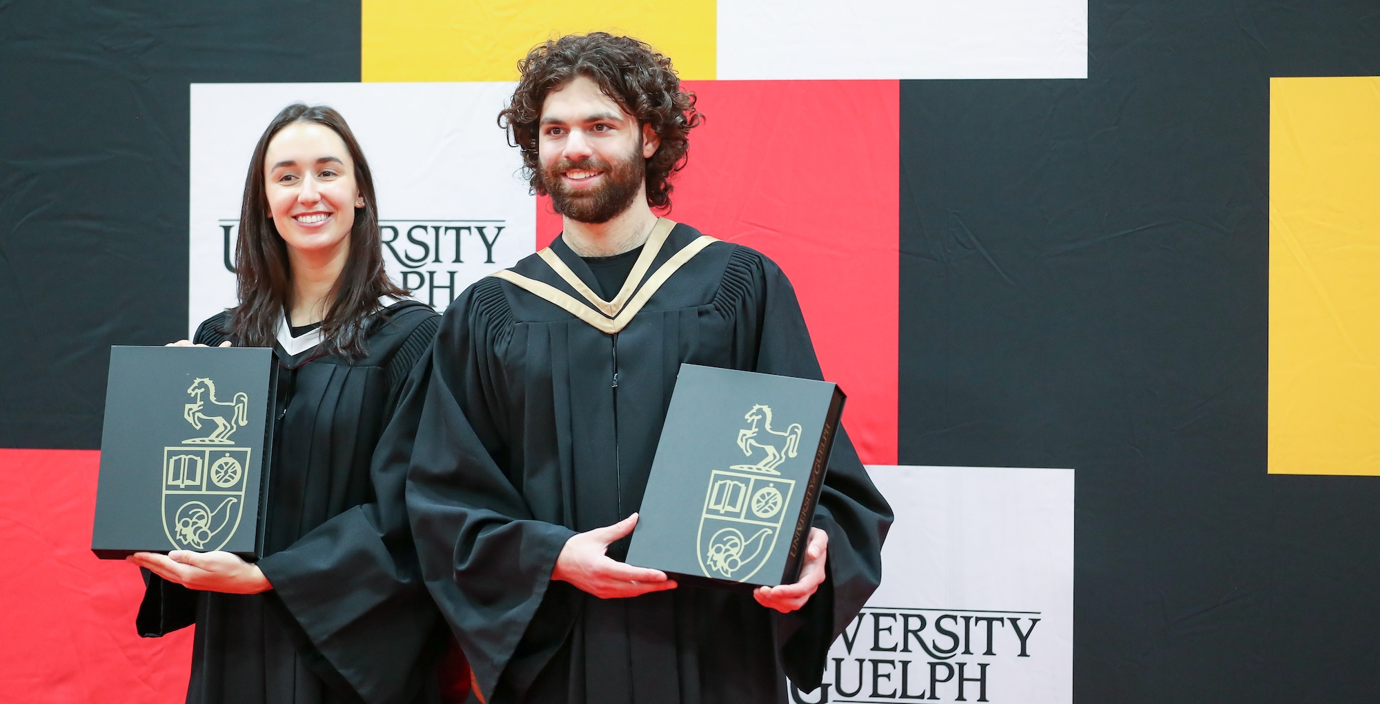 Image of two people smiling at U of G graduate Convocation in their gap and gowns.