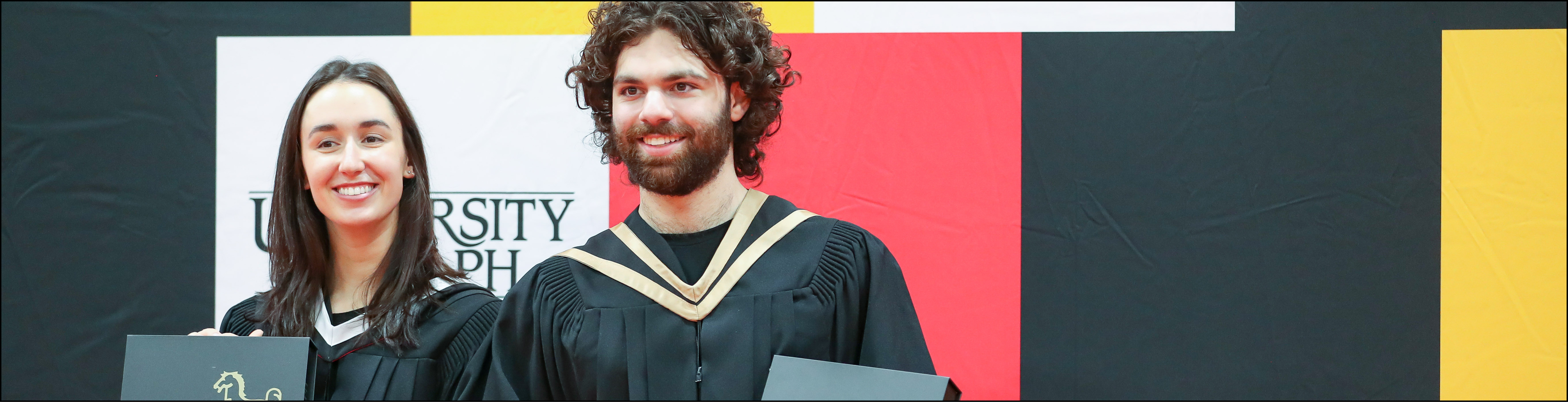 Image of two people smiling at U of G graduate Convocation in their gap and gowns.