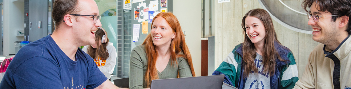 Image of four smiling people sitting at a table in front of a computer.