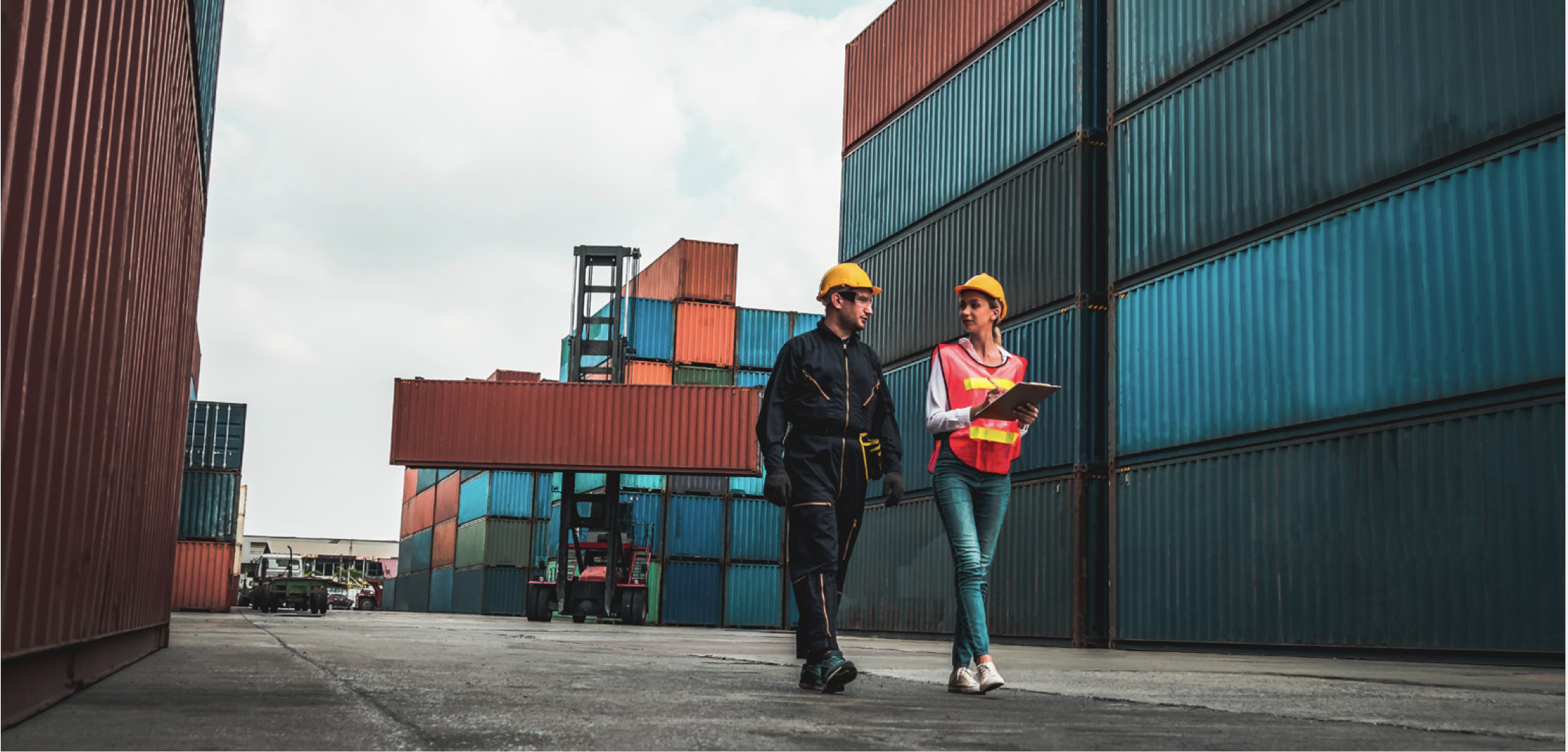 Man and woman in hard hats walking through area with shipping containers
